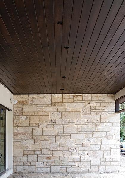 A dark wood plank ceiling contrasts with a light stone wall of rectangular and square blocks, finished with Modern Masters - Masterclear Supreme for lasting protection. A glass window on the left adds to the modern, textured aesthetic.