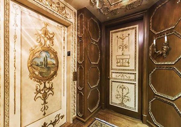 Luxurious room with gold accents, intricate carvings, and classical wall designs. A faux finish created with Modern Masters - Tintable Glaze enhances the space, featuring a central panel displaying a serene landscape painting.