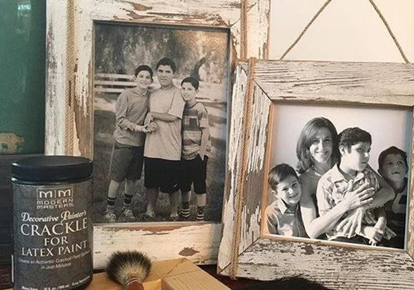 Two framed black-and-white family photos sit on a surface. Nearby, a can of Modern Masters Crackle for Latex Paint, along with a brush and stick, suggests someone plans to give the frames an antique look.
